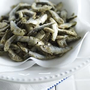 Fried whitebait on kitchen paper in bowl, close-up