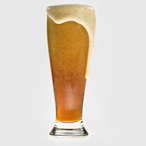 Glass of wheat beer with froth overflowing at the top