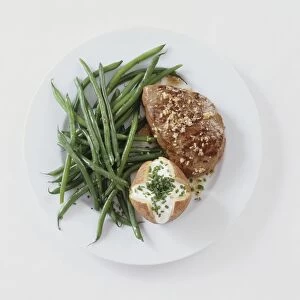 Steak served with baked potato, sour cream, chives and green beans on white plate