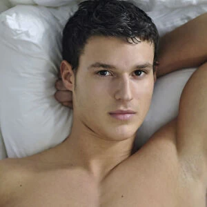 Bare-chested young man lying in bed