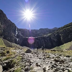 Trekkers walking along the cirque of Gavarnie. Hautes Pyrenees. France. World Heritage by UNESCO, the great waterfall