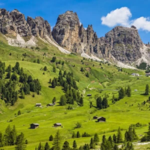 Grassy mountain side with wooden mountain huts and the jagged mountain ridge at the Gardena Pass in the Dolomites in South Tyrol, Italy