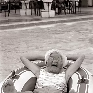 Old woman in an inflatable dinghy in a swimming pool August 1984