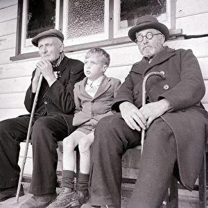 A young boy sits down with two old men on a bench. circa 1940